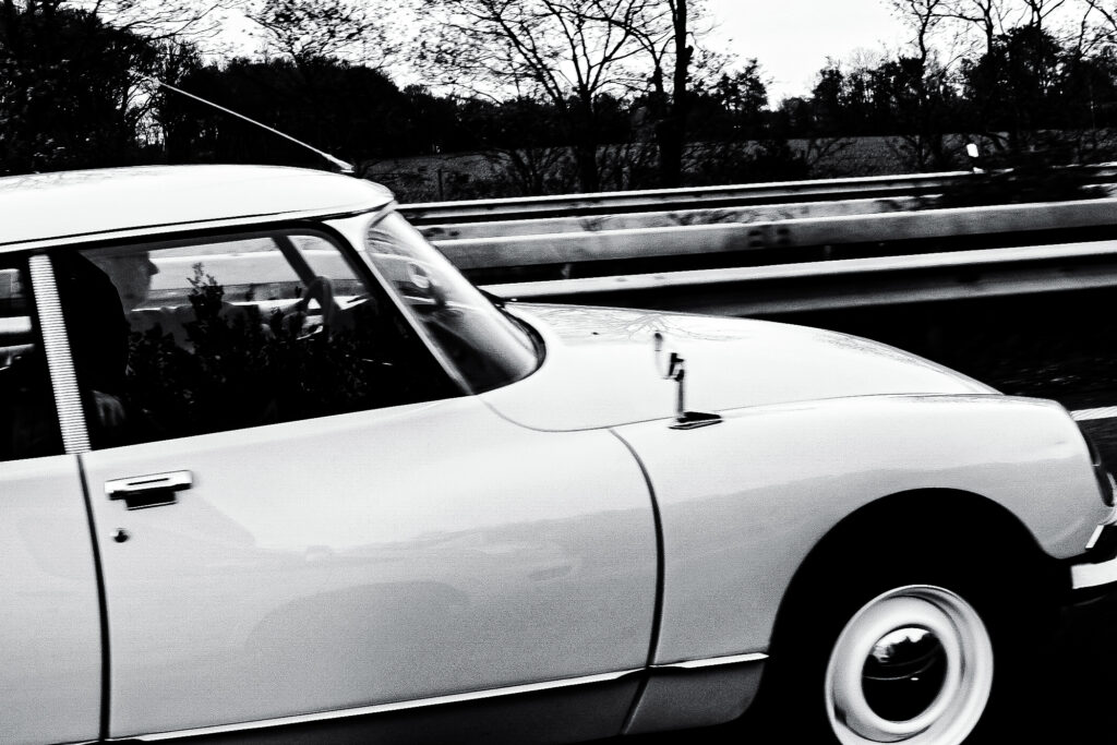 Schwarzweißfotografie eines hellen älteren Autos in Seitenansicht.