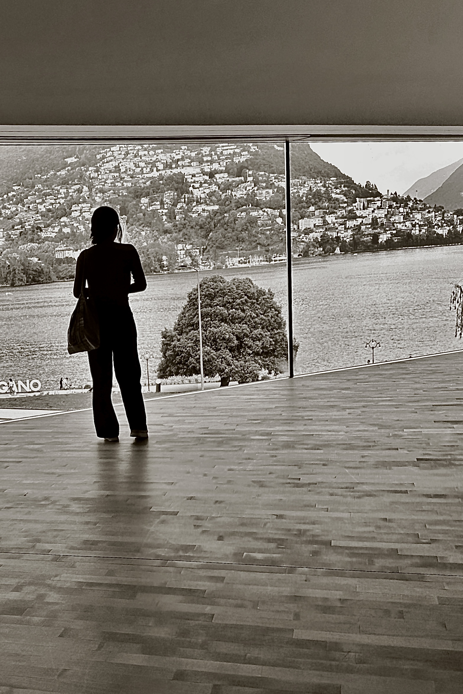Silueta de una persona frente a un gran ventanal con vistas al agua y a varios edificios.